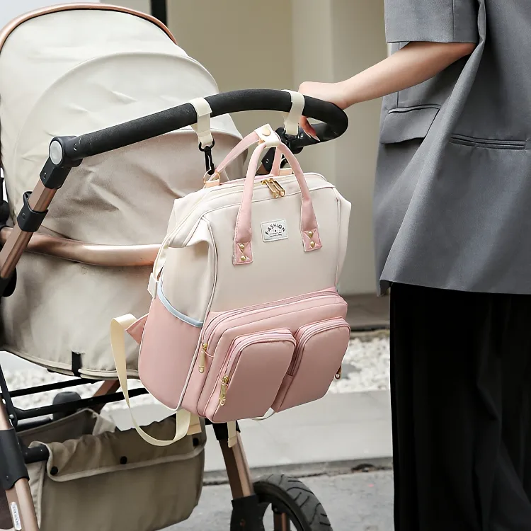 ベビーカーのハンドルに掛けられたクリーム色とピンクの多機能マザーズバッグ。前面ポケットが見えます。