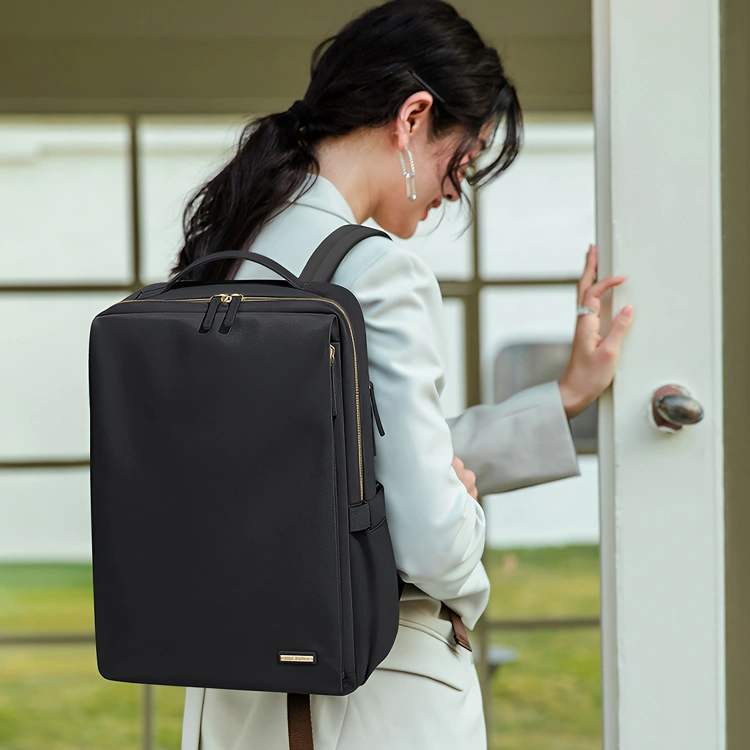 明るいオフィスの入り口でドア枠に手を添えるブレザー姿の女性と、その背にある上品な軽量ビジネスリュック。洗練された大人の通勤シーンです。