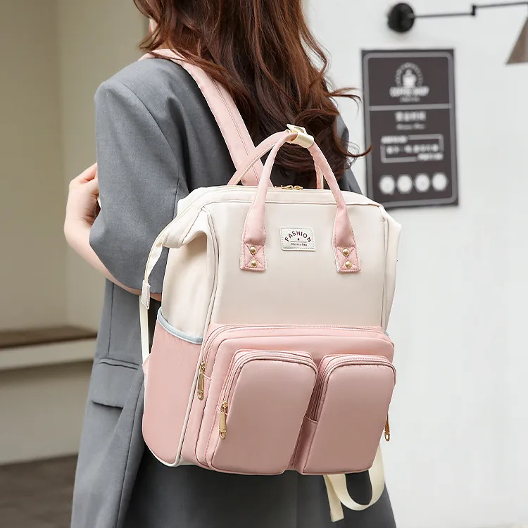 優しいピンクと白のバイカラーリュックを背負った様子。大きな前ポケットとゴールドの留め具がアクセントの、手持ちもできる多機能なデザインです。